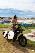 Rider standing with Explorer e-bike and surfboard loaded on the surf rack