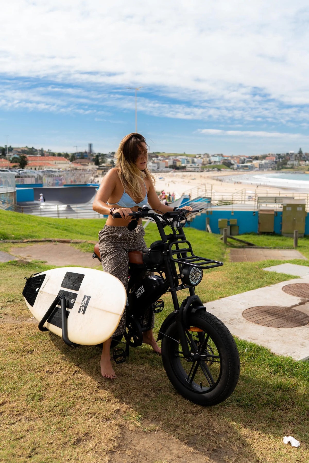 Rider standing with Explorer e-bike and surfboard loaded on the surf rack