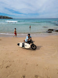 Riding the Explorer e-bike with surfboard on the sand at Bondi Beach