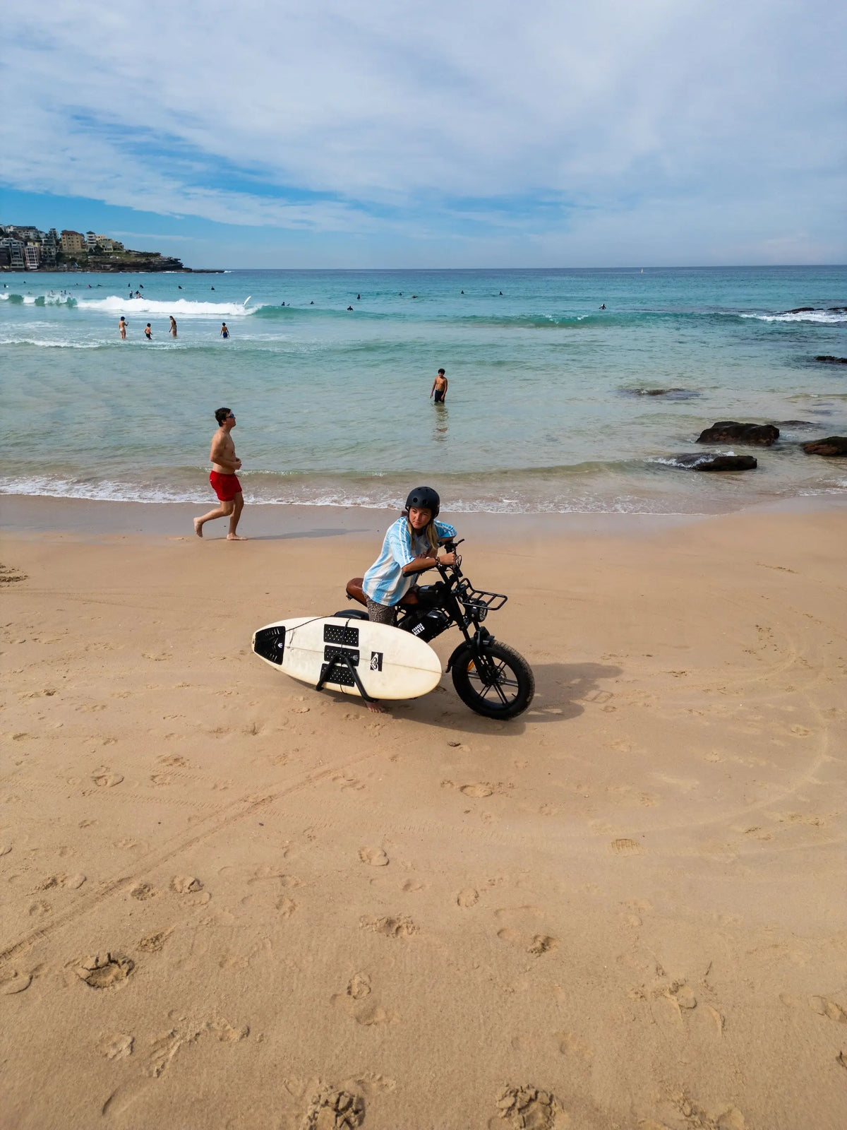 Riding the Explorer e-bike with surfboard on the sand at Bondi Beach