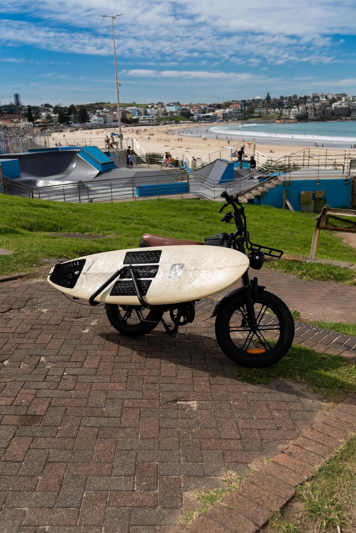 Brown Explorer e-bike with surfboard mounted on the Coogee Bikes surf rack
